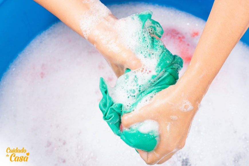 Mulher torcendo roupas em uma bacia após seguir dicas de como deixar roupa de molho