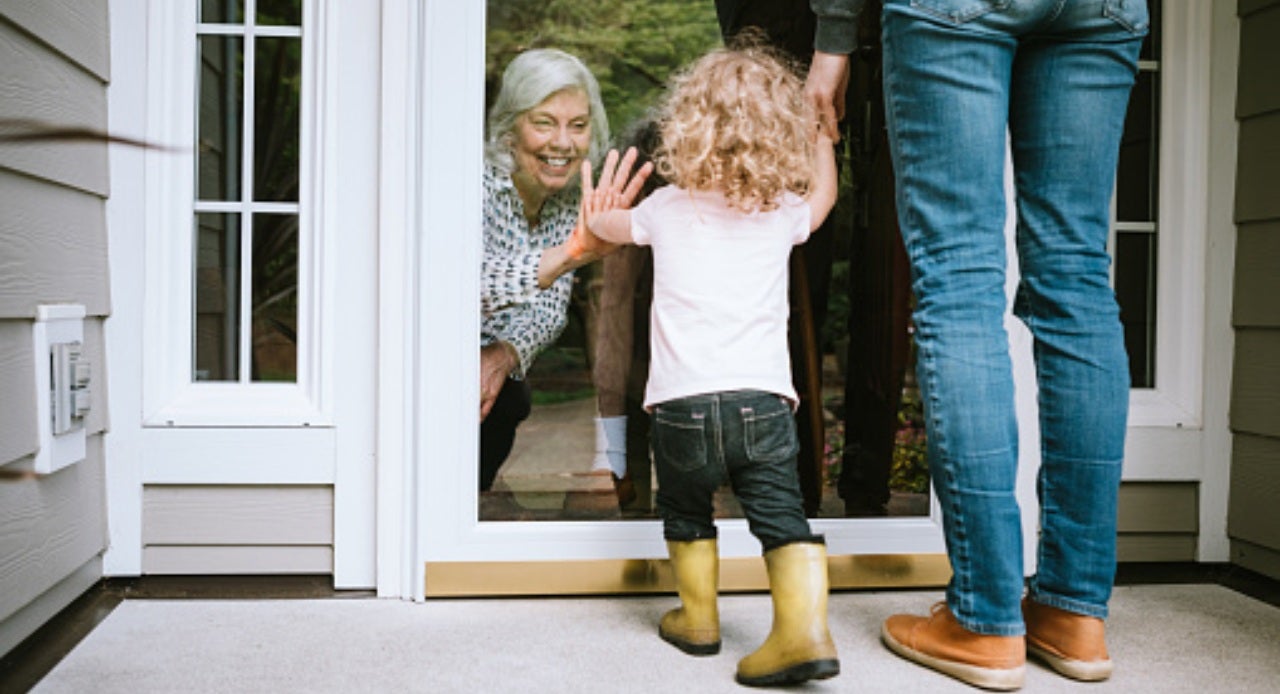 Criança acenando para avó e avô através da porta de vidro, felizes por receber visita em casa
