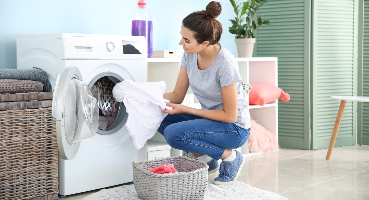 Mulher tirando as roupas limpas da máquina com tranquilidade porque aprendeu como lavar camisa social  