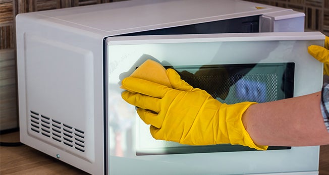 Mão com luva amarela limpando micro-ondas