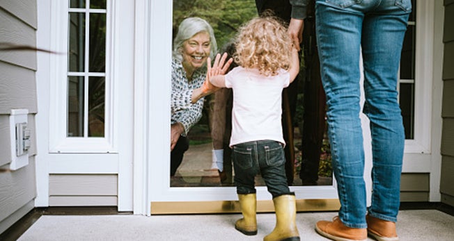 Criança acenando para avó e avô através da porta de vidro, felizes por receber visita em casa